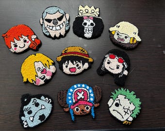 Puede incluir: Una colección de diez posavasos de punch needle con formas variadas que presentan rostros de personajes de dibujos animados, incluyendo figuras con cabello naranja, una calavera con corona, un sombrero de paja y un sombrero azul con cruz rosa.