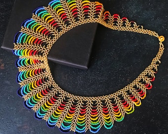 May include: A colourful beaded necklace with a rainbow pattern and gold accents. The necklace is made of small beads and has a scalloped design.