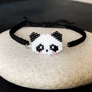 May include: Black beaded bracelet with a white panda face charm. The panda has black eyes and pink cheeks.