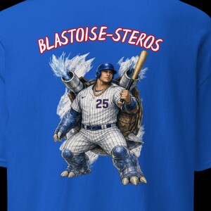 Puede incluir: Camiseta azul real con un gráfico de jugador de béisbol. El gráfico representa a un jugador de béisbol con el número 25, integrado con una criatura parecida a una tortuga. El texto "BLASTOISE-STEROS" está arqueado sobre el gráfico en rojo.