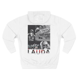 May include: White hooded sweatshirt with a black and white collage of Niki Lauda, a Formula One racing driver. The word "LAUDA" is printed in bold letters at the bottom. The sweatshirt has long sleeves and a kangaroo pocket.