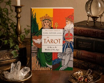 May include: A copy of "The Tarot: A Key to the Wisdom of the Ages" by Paul Foster Case. The book cover features illustrations of figures in green, yellow, and red. A lit candle, crystal ball, and other occult books are in the background.