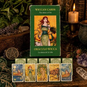以下が含まれることがあります： 「Wiccan Cards」と「The dance of life」と「Oráculo Wicca La danza de la vida」の文字が入った緑色の箱。箱には女性のイラストが描かれています。箱の前には、さまざまなイラストが描かれたいくつかのタロットカードが表示されています。