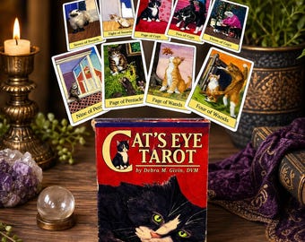 May include: A deck of "Cat's Eye Tarot" cards with a red box featuring a black cat illustration. The deck includes cards with cat illustrations and titles like "Seven of Swords" and "Page of Cups". A candle and crystal ball are also visible.