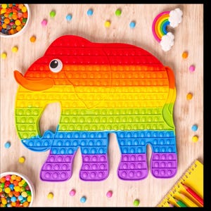 May include: A large, rainbow-colored elephant-shaped pop-it toy. The toy features a gradient of colors, from red to purple, with numerous circular bubbles. A small rainbow and candy are also visible.