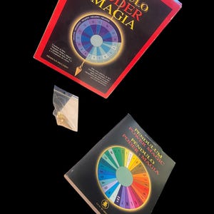 May include: Two books titled "Pendulum Power and Magic" with colorful circular charts and a pendulum. The books have red and black covers with Spanish text. A small, sealed bag containing a gold-colored pendulum is also visible.