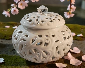 Pote de cerâmica elegante com tampa, branco, com detalhes em strass e decoração vazada.