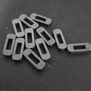 May include: A collection of small, dark gray, rectangular objects with a hollow center. The objects are scattered on a dark surface. The shape of the objects is a rectangle with rounded corners.