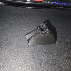 May include: A black plastic phone stand with a triangular base and two adjustable arms. The stand is designed to hold a phone in a vertical position.