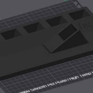 May include: A black 3D printed object with multiple rectangular slots and a triangular cutout. The object is labeled "L17K" and is sitting on a gray grid surface with the text "Smooth PEI Plate/High Temp Plate".