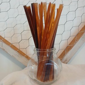 May include: A glass jar filled with a variety of honey sticks. The sticks are a mix of light and dark brown colors.