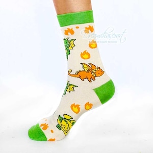 May include: Cream-coloured socks patterned with cartoon dragons in orange, green, and yellow, and orange flames. The top and toe of the socks are green.