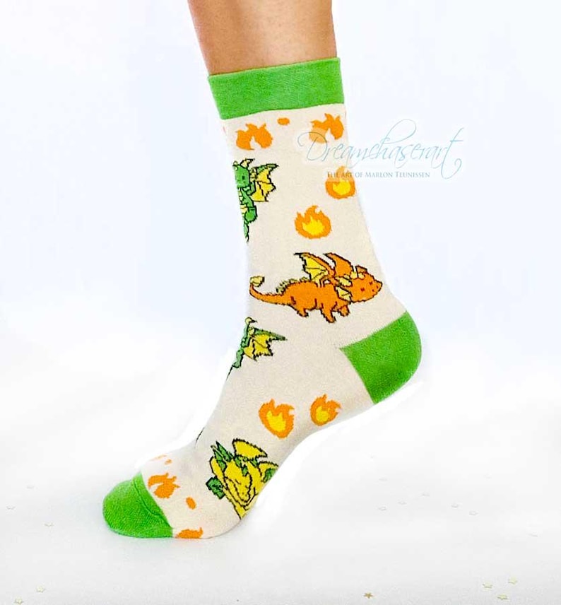 May include: Cream-coloured socks patterned with cartoon dragons in orange, green, and yellow, and orange flames. The top and toe of the socks are green.