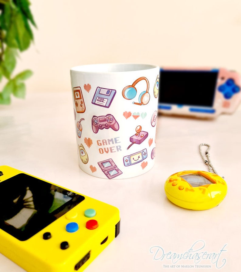 Pu&ograve; includere: Una tazza in ceramica bianca con un design colorato di icone di videogiochi retr&ograve;, tra cui controller, cuffie e una cartuccia di gioco. Il testo "GAME OVER" &egrave; stampato in lettere pixelate sulla tazza.