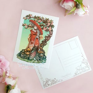 May include: A postcard featuring a woman in a red and white kimono standing in a forest of mushrooms. The woman is holding a large mushroom in her hand and is wearing a large red hat. The postcard has a green and blue background with a tree in the background. The text "Dreamchaser Art" is at the bottom of the postcard.