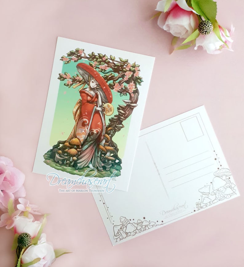 May include: A postcard featuring a woman in a red and white kimono standing in a forest of mushrooms. The woman is holding a large mushroom in her hand and is wearing a large red hat. The postcard has a green and blue background with a tree in the background. The text "Dreamchaser Art" is at the bottom of the postcard.