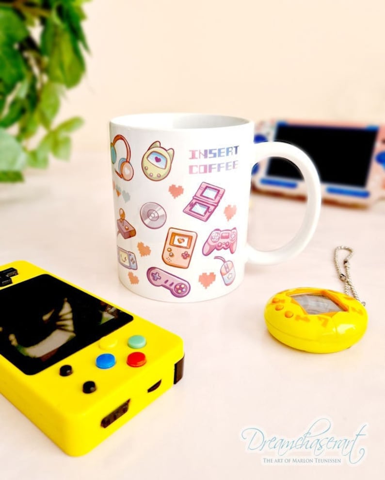 Pu&ograve; includere: Una tazza in ceramica bianca con un design rosa e blu con icone retr&ograve; di videogiochi e tecnologia. La tazza ha il testo "Insert Coffee" sul davanti.