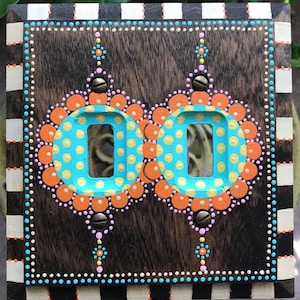 May include: A double light switch cover with a woodgrain finish. The cover is decorated with hand-painted polka dots in shades of orange, yellow, blue, and pink.