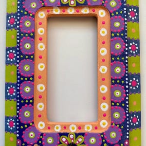 May include: Hand-painted rectangular picture frame with a vibrant floral design. The frame features a peach-colored inner border and is adorned with colorful flowers, dots, and geometric patterns in shades of blue, green, purple, and white.
