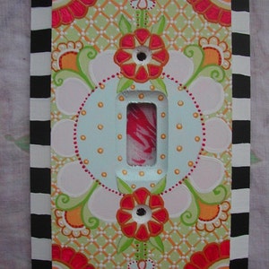 May include: A hand-painted light switch cover with a floral design. The cover features a white background with pink, red, orange, and green flowers. The cover is framed with a black and white checkered border.