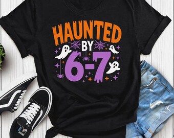 May include: Black t-shirt with the text "HAUNTED BY 6-7" in orange and purple, featuring ghost and spider graphics. The shirt is paired with denim shorts and black sneakers.