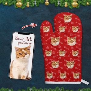 May include: Red oven mitt with a white border. The mitt has a repeating pattern of paw prints and fish bones. The pattern is filled with images of a cat's face. The text "Your Pet picture" is on a phone screen in the background.