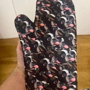 May include: Black oven mitt with a repeated pattern of French Bulldog faces. The dogs have black and white fur and are sticking their tongues out.