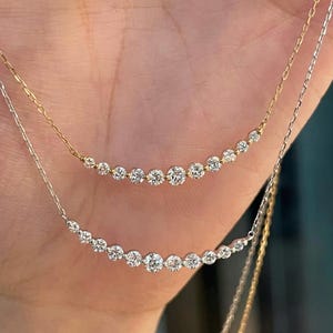 May include: Two elegant necklaces, one gold and one silver, each featuring a row of diamonds. The diamonds are set in a curved line. The necklaces are shown against a neutral background. The diamonds sparkle, catching the light.