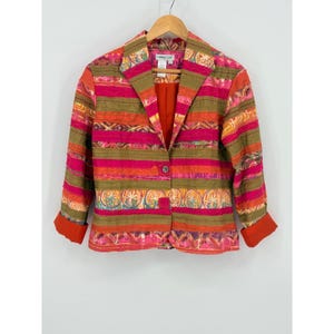 May include: A long-sleeve blazer featuring horizontal stripes in shades of olive green, bright pink, and orange. The garment has a notched lapel, a single button closure, and solid orange cuffs. The fabric displays a mix of solid bands and patterned sections with circular and geometric motifs.
