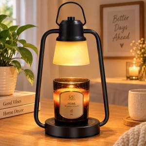 May include: A black metal candle warmer lamp with a handle and a frosted glass shade. The lamp illuminates a dark glass candle jar with a beige label that reads RE CLASSIFIED HEBE the goddess of youth 200g. The base is circular and black.