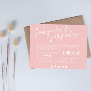 May include: A pink thank you card with white script that reads "Thank you for your purchase." The card includes a heart symbol and social media icons. A brown envelope is behind the card. Dried flowers are in the background.