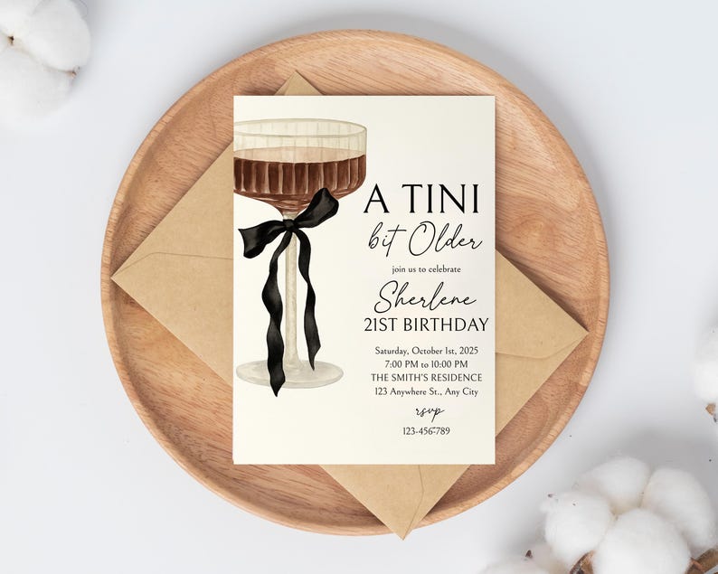 Puede incluir: Una tarjeta de invitaci&oacute;n con el texto "A Tini bit Older" y "Sherlene 21st Birthday". La tarjeta presenta una ilustraci&oacute;n de acuarela de una copa de c&oacute;ctel con una cinta negra. La tarjeta est&aacute; sobre un plato de madera con un sobre.