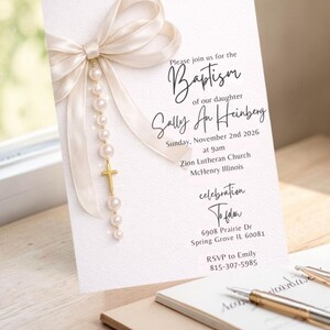 Puede incluir: Invitaci&oacute;n de bautizo con lazo color crema y detalles de perlas. La invitaci&oacute;n incluye el texto "Please join us for the Baptism of our daughter Sally An Heinberg" y detalles del evento. Una cruz dorada cuelga del lazo.