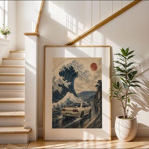 May include: A framed art print featuring a white sports car driving on a coastal road beneath a large stylized blue ocean wave and a red sun, with a mountain visible in the background, all rendered in a traditional Japanese woodblock print style.