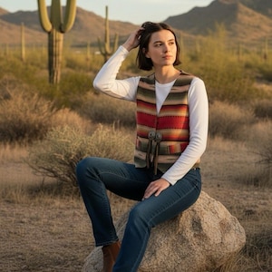 May include: A colorful, striped vest with a Southwestern design. The vest features red, green, and tan stripes and is paired with a white long-sleeve shirt and blue jeans. Brown leather boots complete the look.