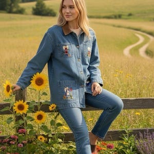 May include: A denim jacket and jeans outfit with embroidered details. The jacket features a brown corduroy collar and pocket embroidery. The person is leaning on a wooden fence with sunflowers and angel statues in a field.