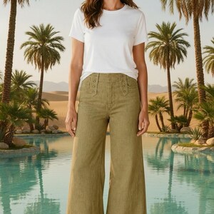 May include: A plain white short-sleeved t-shirt paired with olive green high-waisted wide-leg trousers. The trousers feature a structured waistband with two vertical rows of three buttons on each side of the front, creating a distinct military-inspired look.