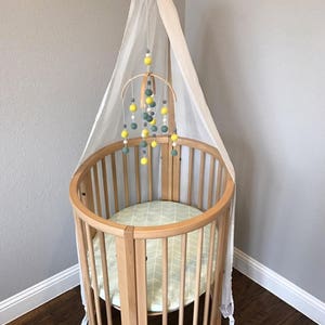 May include: A wooden baby crib with a white canopy and a yellow and green felt ball mobile hanging above it.