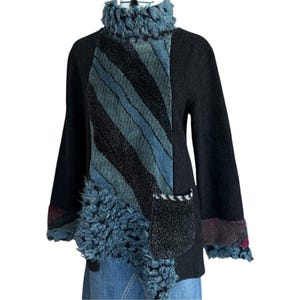 Könnte beinhalten: Schwarzer Pullover mit einem einzigartigen Design. Er hat eine blau-grau gestreifte Bahn, Kunstfell-Details und eine strukturierte Tasche. Der Pullover hat einen Rollkragen und lange Ärmel mit gemusterten Bündchen. Ein modisches und warmes Kleidungsstück.