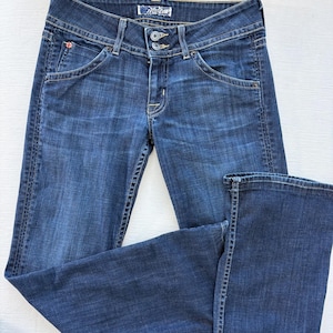 Może przedstawiać: Ciemnoniebieskie dżinsy z klasycznym pięciokieszeniowym designem. Posiadają zapięcie na guzik i zamek błyskawiczny oraz mały czerwony emblemat na przedniej kieszeni. Dżinsy są złożone, prezentując tylne kieszenie i metkę marki.