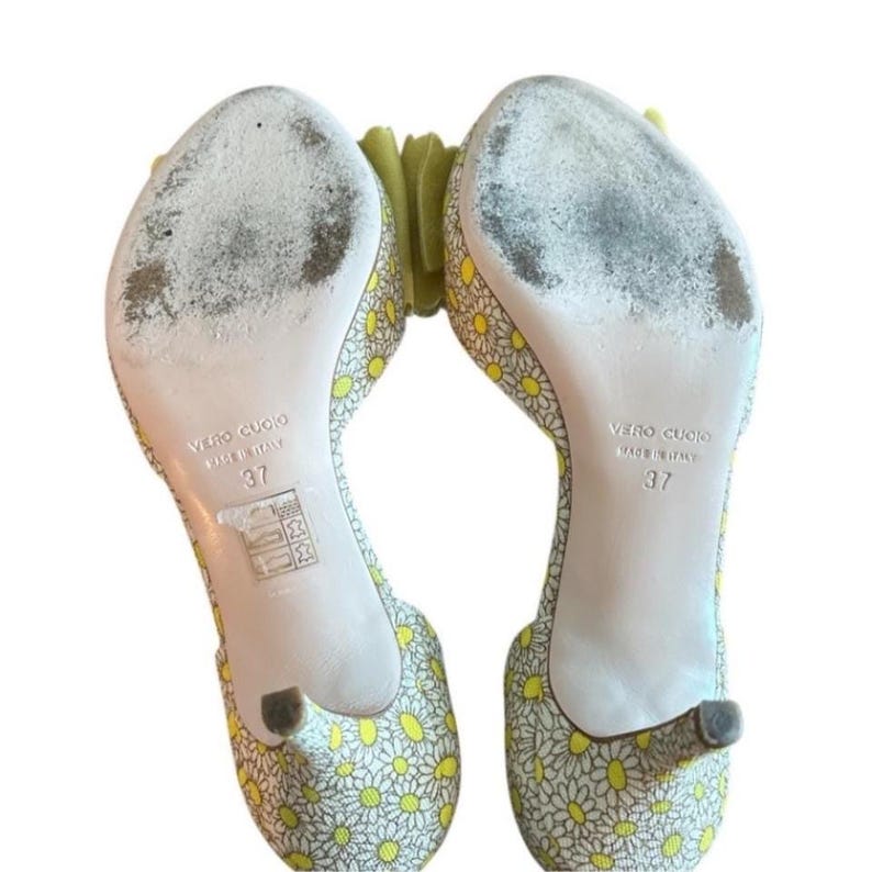 Op de afbeelding: Een paar open teen hakken met een bloemenpatroon. De schoenen hebben een gele en witte madeliefjesprint op een lichte achtergrond. De zolen zijn gemarkeerd met "VERO CUOIO MADE IN ITALY" en maat 37.