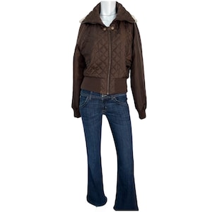 Może przedstawiać: Brązowa pikowana kurtka bomberka z zapięciem na zamek błyskawiczny, połączona z ciemnoniebieskimi dżinsami. Kurtka ma prążkowany d&oacute;ł i mankiety oraz kołnierz z jasnym wykończeniem. Dżinsy mają rozszerzaną nogawkę.