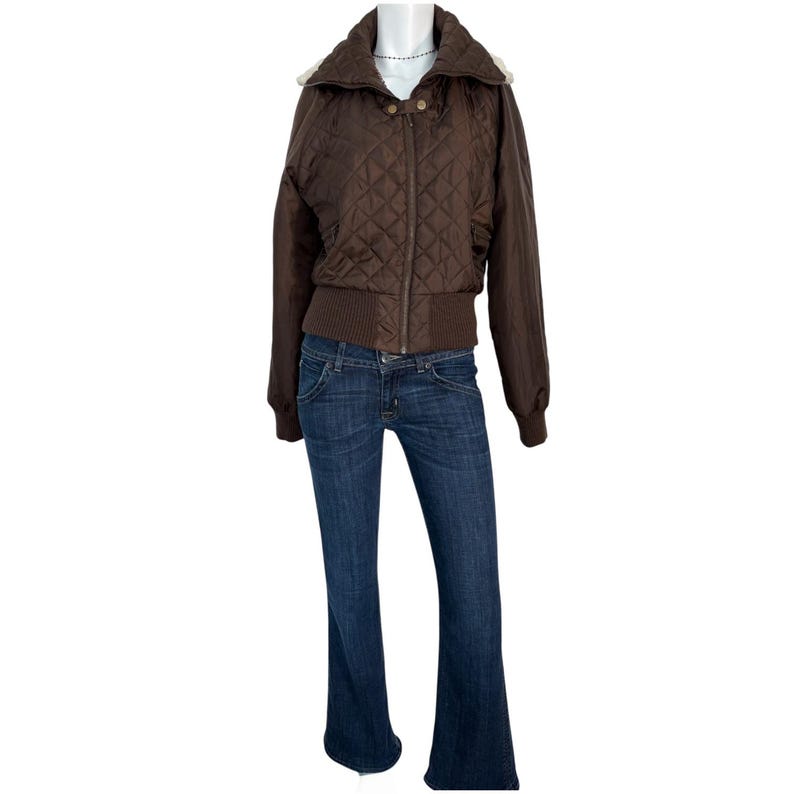 Może przedstawiać: Brązowa pikowana kurtka bomberka z zapięciem na zamek błyskawiczny, połączona z ciemnoniebieskimi dżinsami. Kurtka ma prążkowany d&oacute;ł i mankiety oraz kołnierz z jasnym wykończeniem. Dżinsy mają rozszerzaną nogawkę.