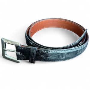 May include: Black textured belt with a silver buckle. The belt has a reptile-like pattern on the exterior and a brown interior. The buckle is rectangular and has a shiny finish. The belt is designed to be worn around the waist.