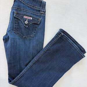 Może przedstawiać: Ciemnoniebieskie dżinsy z klasycznym pięciokieszeniowym designem. Dżinsy mają zapięcie na guzik i zamek błyskawiczny, szlufki na pasek i małą kieszeń z przodu. Tylna kieszeń ma dekoracyjny wz&oacute;r.