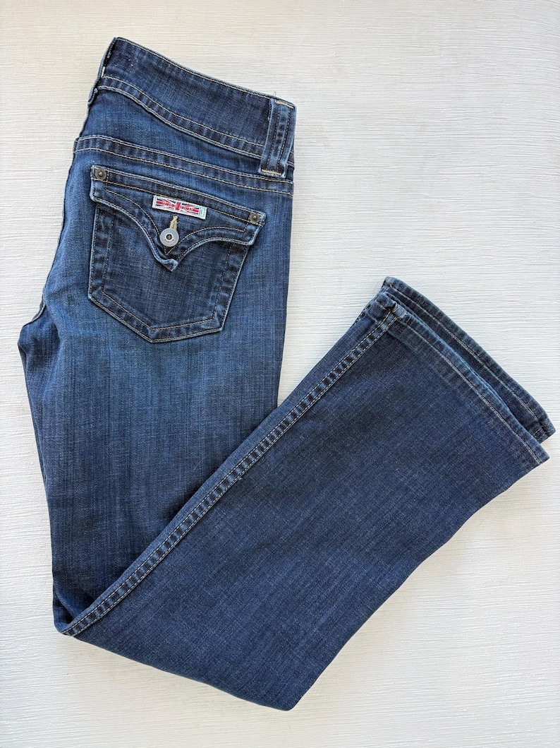 Może przedstawiać: Ciemnoniebieskie dżinsy z klasycznym pięciokieszeniowym designem. Dżinsy mają zapięcie na guzik i zamek błyskawiczny, szlufki na pasek i małą kieszeń z przodu. Tylna kieszeń ma dekoracyjny wz&oacute;r.