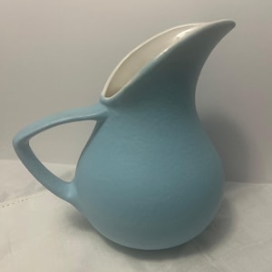 May include: A light blue ceramic pitcher with a textured surface. The pitcher has a curved handle and a spout with a white interior. The pitcher is likely used for serving beverages.