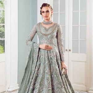 May include: A sage green formal gown with intricate silver embroidery and beading. The long-sleeved dress features a V-neckline, a full skirt, and a matching sheer shawl. A small clutch completes the elegant ensemble.