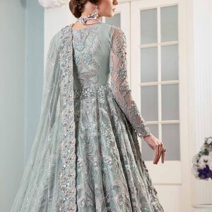 May include: A pale green formal gown with detailed silver embroidery and embellishments. The long-sleeved dress has a flowing skirt and a sheer, embellished cape. Suitable for special occasions.