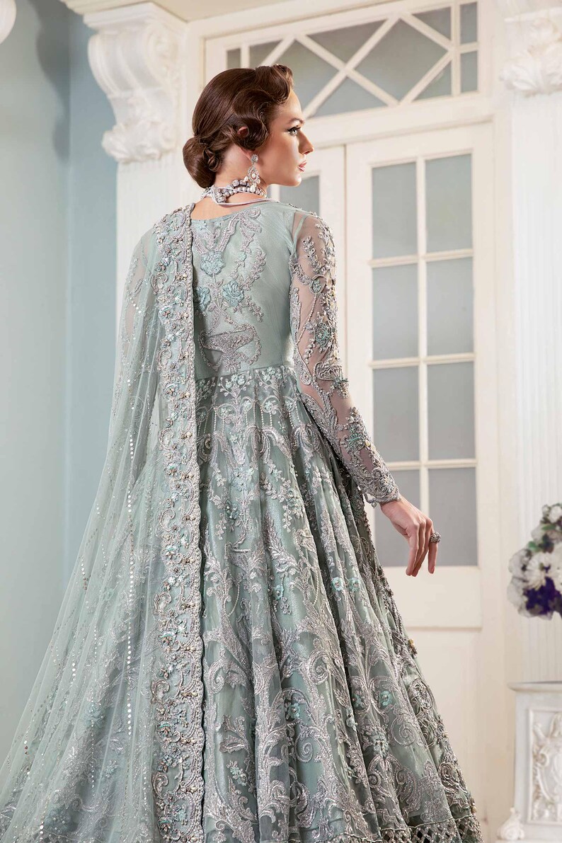 May include: A pale green formal gown with detailed silver embroidery and embellishments. The long-sleeved dress has a flowing skirt and a sheer, embellished cape. Suitable for special occasions.